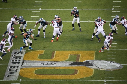 Cam Newton (1) drops back for a pass near the 50-yard line. The large Super 50 logo looms in the foreground